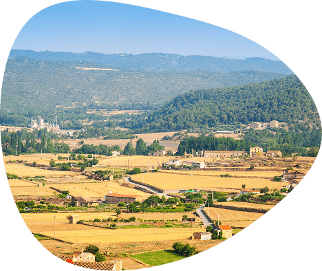 Vue d'une vallée avec une ville située au loin, entourée de collines verdoyantes sous un ciel dégagé.